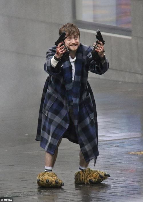 accio-shitpost:
“ so the new harry potter movie looks interesting
[Image: a picture of Daniel Radcliffe wearing a blue checked dressing gown and tiger paw slippers. He is standing outside on a rainy pavement. He is holding a gun in each hand and is...
