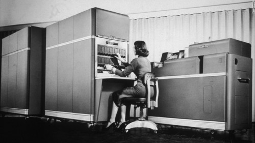 A woman operates one of the early desktop IBM computers in...