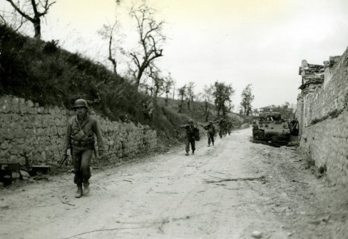 historicaltimes:US mortar men walk past a Sherman tank knocked...