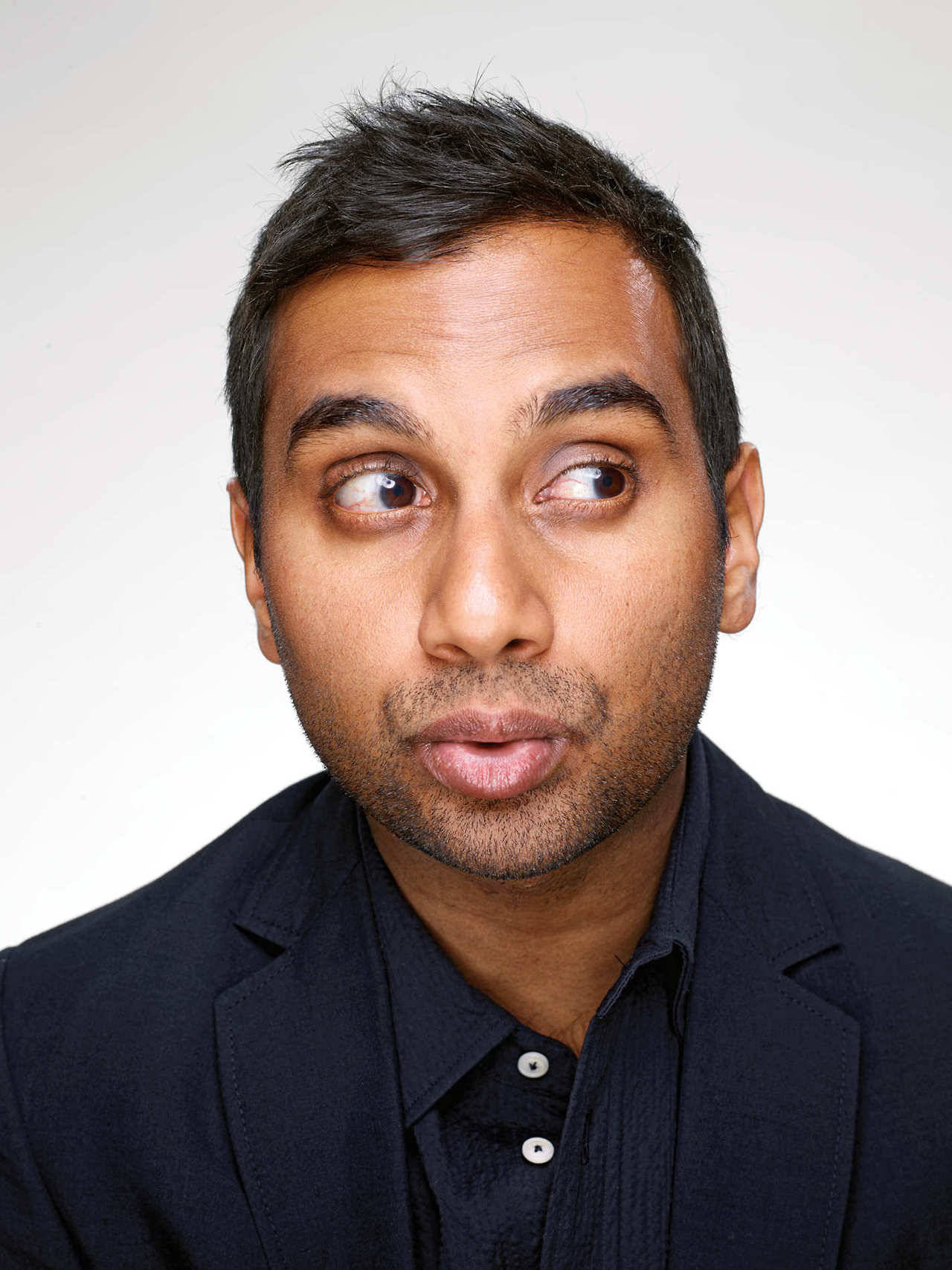 Close-up of Aziz Ansari whistling, wearing a Brooklyn Tailors jacket and shirt