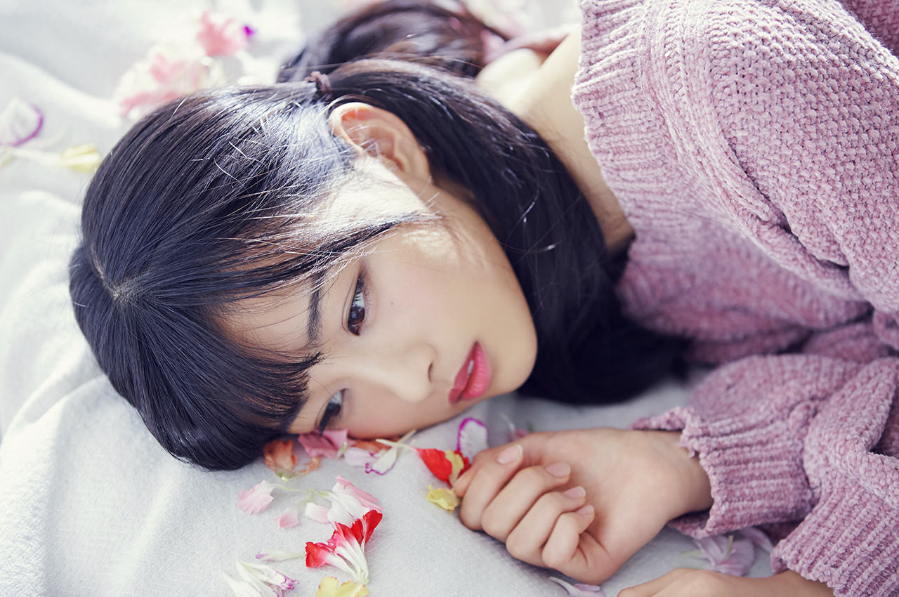ピンクのニットワンピを着て花弁の上に寝ている原田葵の画像