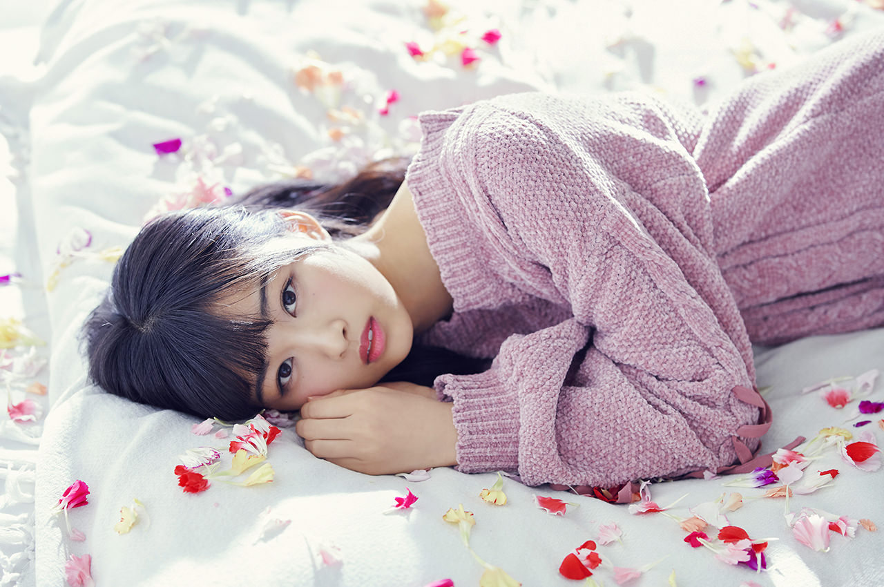 ピンクのニットワンピを着て花弁がちりばめられたベッドに横になる原田葵の画像