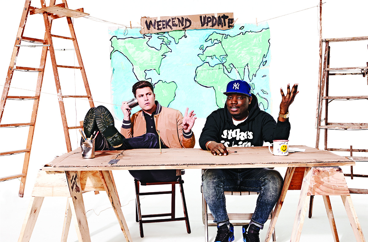Colin Jost and Michael Che sit at a news desk in Brooklyn Tailors